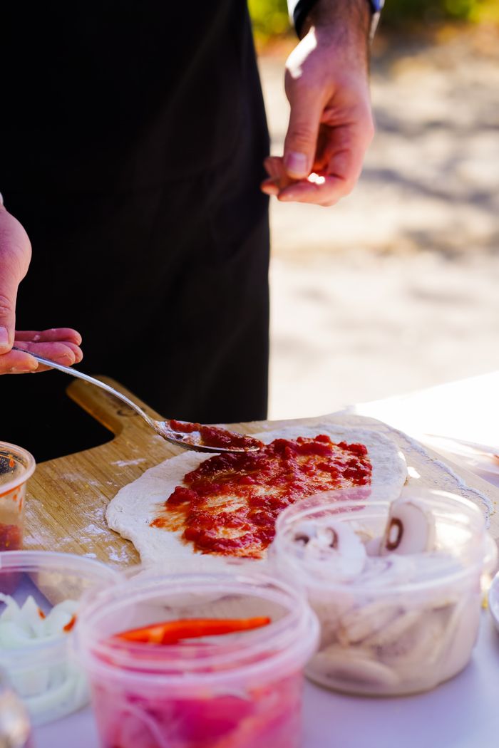 An artisan spreads sauce on pizza dough, preparing a delicious meal.